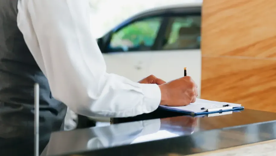 Pessoa assinando documento sobre prancheta ao lado de um carro